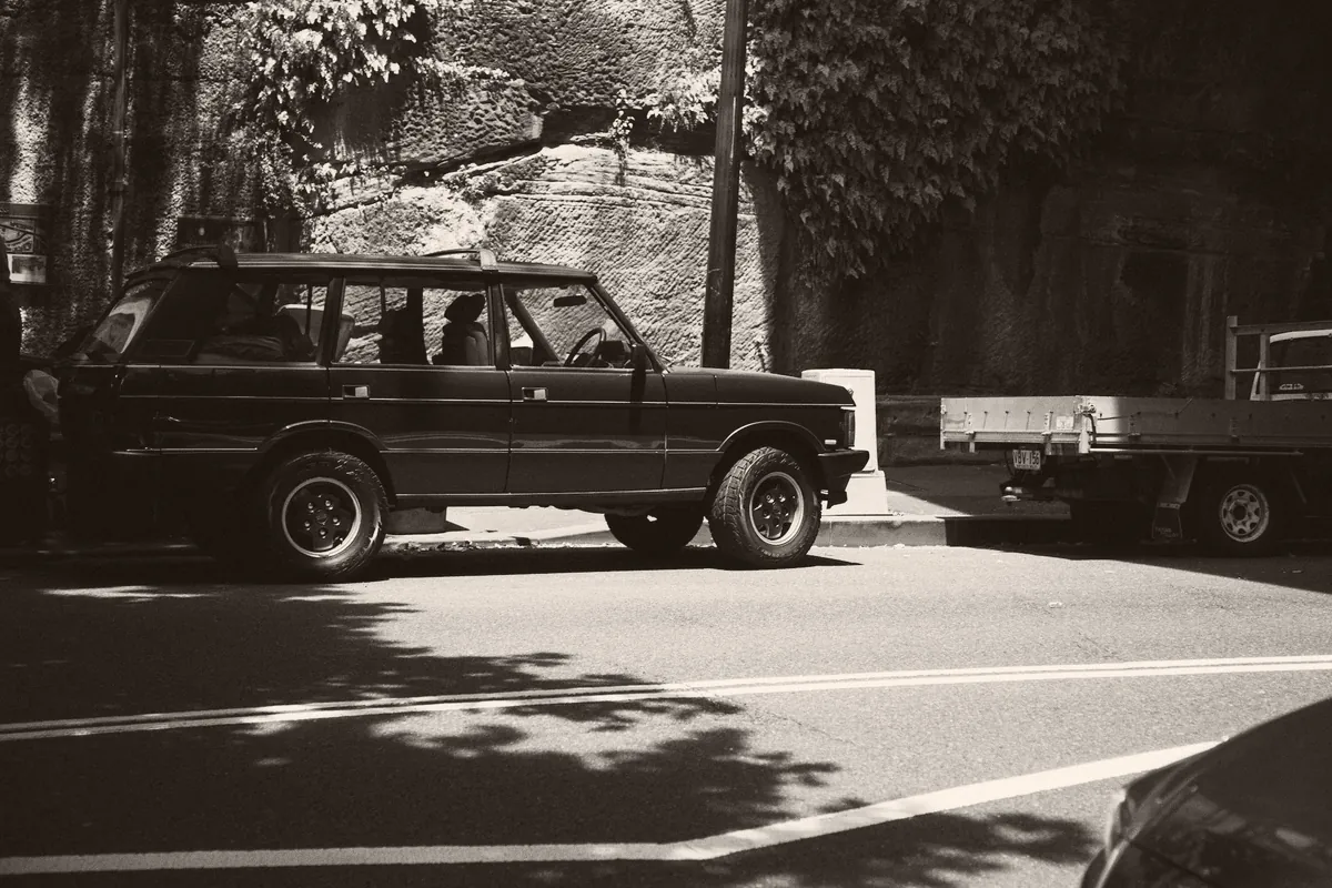 A classic Range Rover parked on a street below a sandstone wall