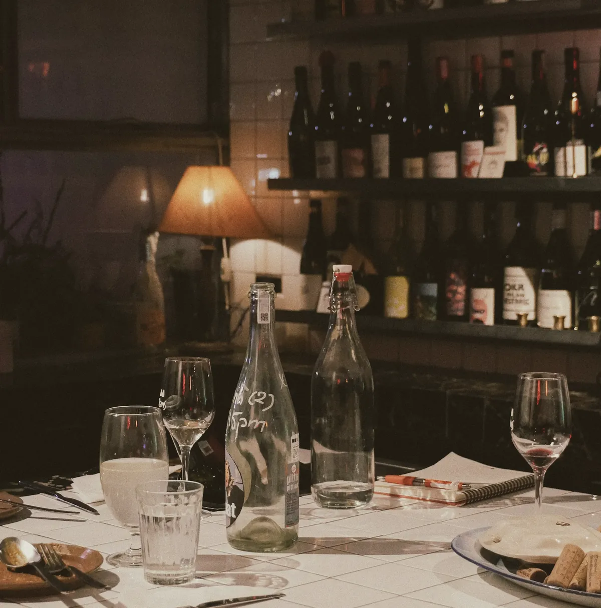 A table after dinner, empty glasses and bottles still out, corks on a plate